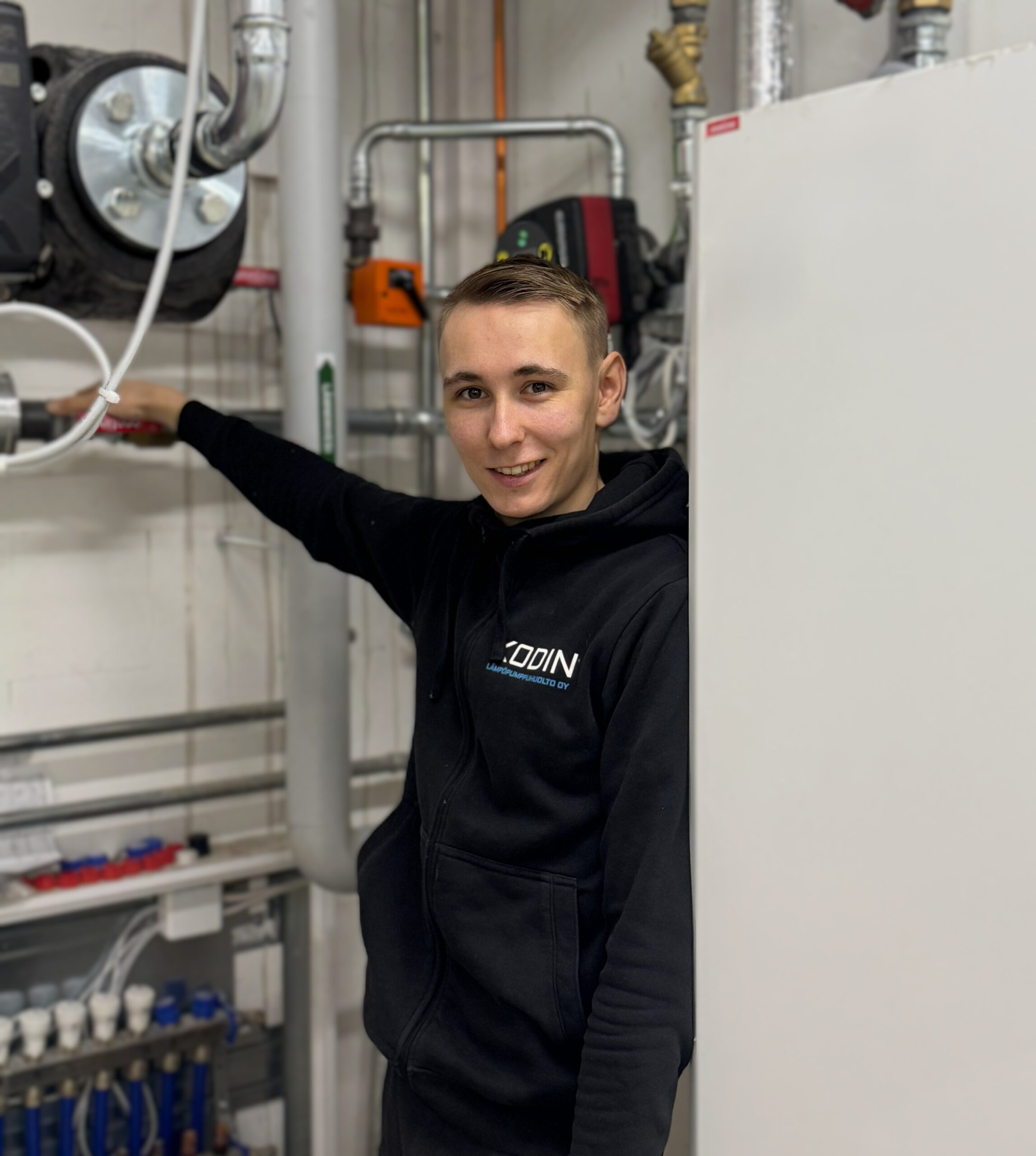 Eelis, Vastuu Energian asentaja, mustassa hupparissa, putkistotöissä lämmitysjärjestelmän äärellä