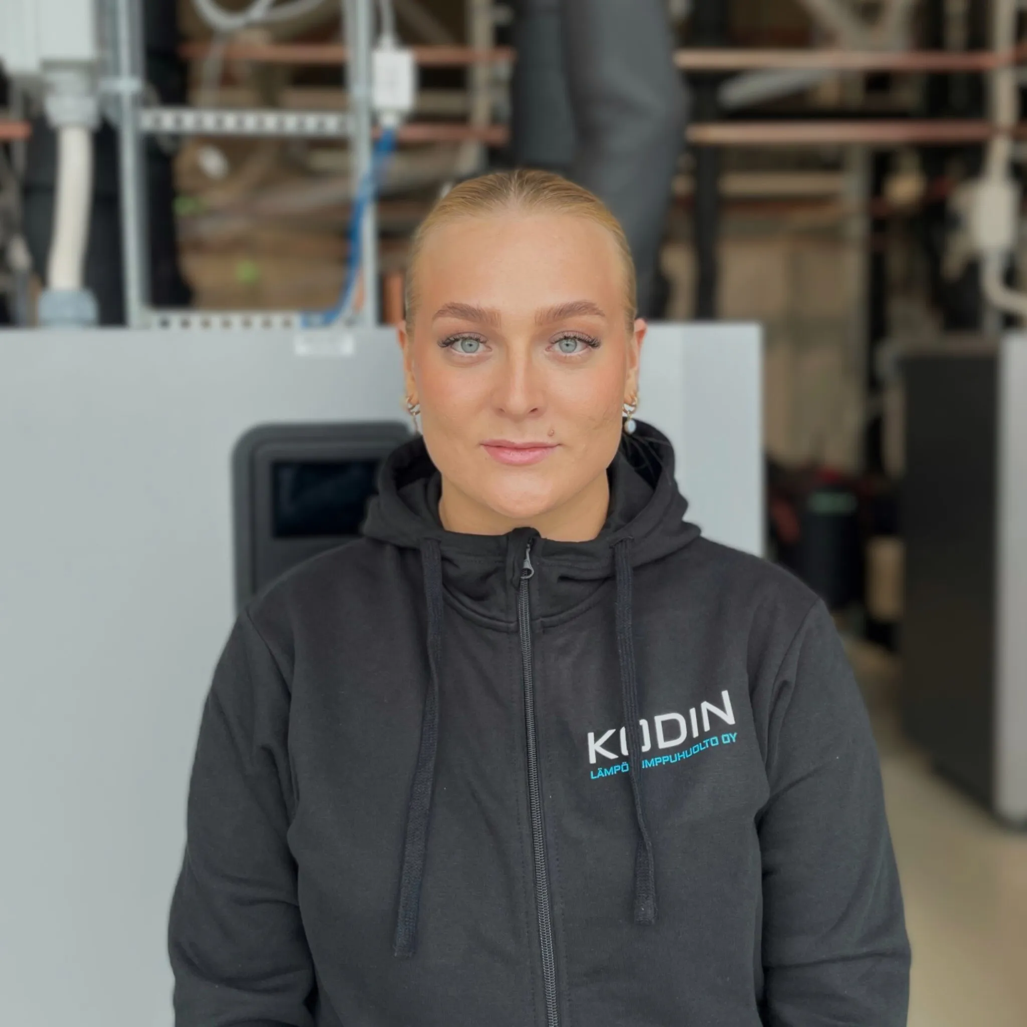 Iida-Maria, Vastuu Energian työntekijä, mustassa yrityksen hupparissa, lämpöpumpun edessä